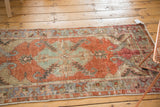 Distressed Oushak runner's faded cherry red field, slate blue serrated medallion, and visible wear.