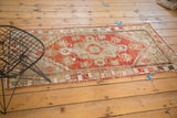 Corner view of a vintage distressed Oushak rug, showing wear, secured edge, and fringed end.