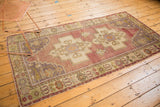 Oushak rug corner reveals faded sage, aubergine, and ivory floral border details.