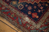 Finely woven antique Heriz rug corner with elaborate red border, indigo field, and threadbare foundation.