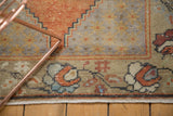 Distressed Vintage Oushak rug corner with faded orange palmettes and worn geometric pile.