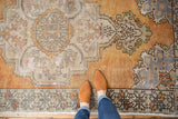 Distressed Oushak rug corner showing faded tangerine, rust, ivory Rococo spandrel and wear.