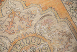 Distressed Oushak carpet's worn texture, showing faded tangerine, ivory, rust, and slate blue.