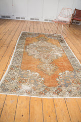 Distressed Oushak carpet's secured end, faded tangerine, ivory, and slate grey tones, with wear.
