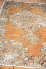 Distressed Oushak carpet corner, showing worn pile with faded tangerine, ivory, and slate blue.