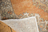 Curled corner view of vintage Oushak rug, showing worn tangerine pile and hand-knotted foundation.