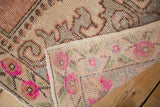Distressed Oushak pile with bright pink floral motifs, revealing hand knotted rug backing.