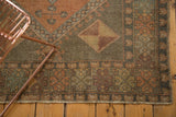 Distressed Turkish Oushak rug corner, geometric motifs in faded aubergine, bronze, and saffron.