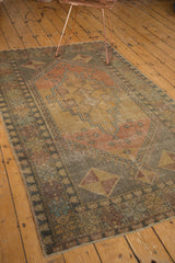 Corner of distressed Oushak rug with time-softened green, terra cotta, and bronze pinwheel motif.