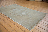 Distressed vintage Oushak rug corner, showing low pile, foundation, and faded bronze border.