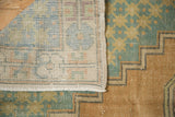 Vintage distressed Oushak rug corner showing hand-knotted foundation, fringed end, faded teal pattern.