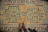 Distressed Oushak rug with dusty gold, sage green, and blue rectilinear double medallion.