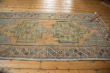 Distressed Oushak rug corner, revealing worn pile, geometric border, and muted gold-green palette.