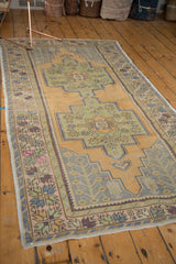 Distressed Oushak rug, rectilinear gold field, sage medallion, and blue-violet plant motifs.