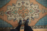 Distressed Oushak rug's scalloped central medallion in soft aqua, gold, ivory, and aubergine under boots.