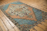 Distressed corner of an Oushak rug runner, showing pale aqua field and celadon, aubergine floral border.