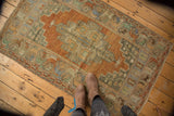 Distressed vintage Oushak rug with muted terra cotta field, celadon spandrels, and wide floral border.