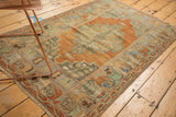 Distressed Oushak rug with soft terra cotta field, muted green spandrels, and floral border.