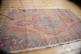 Distressed Oushak rug corner showing faded floral border, slate blue, blush, and beige tones.