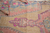 Detail of distressed vintage Oushak rug, showing stylized finial motif in vivid pink, beige, and slate blue.