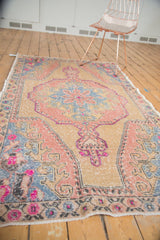 Distressed Oushak rug corner, showing even wear, blush, slate blue, and faded violet floral motifs.