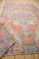 Decorative distressed Oushak rug corner with faded tangerine, fuchsia, blue, and ivory primitive florals.