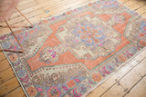Faded tangerine orange distressed vintage Oushak rug corner with blue and pink floral motifs.
