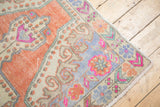 Faded tangerine, slate blue, and fuchsia plant motifs on worn Oushak rug corner.