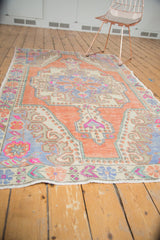 Oushak rug end with faded tangerine orange, pink, and blue primitive floral designs.