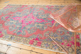 Distressed vintage Oushak rug featuring a scalloped medallion, vibrant pinks, slate blue, and beige.
