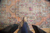 Distressed Oushak rug section featuring faded burnt orange, curvilinear ivory, and fuchsia patterns.