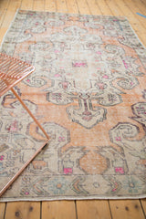 Distressed Oushak rug showing scalloped medallion, faded burnt orange, ivory, and bright pink tones.
