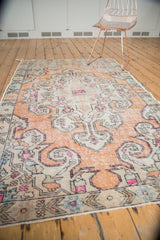 Distressed Oushak rug corner showing faded burnt orange, ivory, and pink scrolling spandrel.