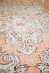 Distressed vintage Oushak rug showing faded burnt orange, ivory, and fuchsia scrolling details.