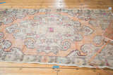 Distressed Oushak rug corner with faded burnt orange field, antique ivory spandrel, and pink accents.