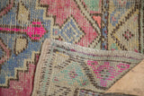 Distressed Oushak rug corner showing bright pink, blue, green motifs and hand-knotted reverse.
