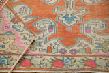 Distressed vintage Oushak rug, terra cotta field, ivory scrolls, slate blue, and vibrant pink motifs.