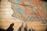 Distressed Oushak rug's rolled edge: faded tangerine, blue geometric border, low pile.