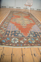 Distressed Oushak runner's lower section: floral border, slate blue plant spandrels, madder red field.
