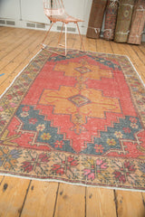 Distressed Oushak rug's pale cranberry field, floral dusty gold border, and intact fringe.