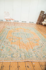 Distressed Oushak carpet with worn pile, showcasing faded tangerine, blue, and ivory patterns.