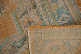 Folded corner of a distressed Oushak rug, showing secured edge, exposed foundation, and soft colors.