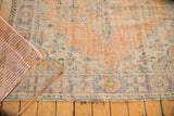 Distressed vintage Oushak rug corner with worn tangerine pile and faded blue, ivory border.