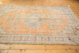Distressed Oushak rug corner, showing faded tangerine, blue floral patterns, and exposed foundation.