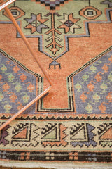 Distressed Oushak runner's geometric border and boteh spandrels in apricot, celadon, and blue.