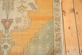 Distressed Oushak rug corner showing stepped spandrel with pale orange, celadon, and ivory motifs.