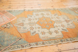 Distressed vintage Oushak rug corner showing stepped spandrel, floral border; ivory, orange, aqua.