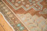 Distressed vintage Oushak rug corner showing bronze field, germinating plants, and white fringe.