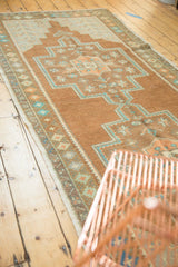 Distressed Oushak rug runner featuring textured bronze, teal, and copper floral border.