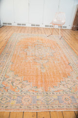 Distressed vintage Oushak rug corner with apricot field, pale blue floral spandrel and border.